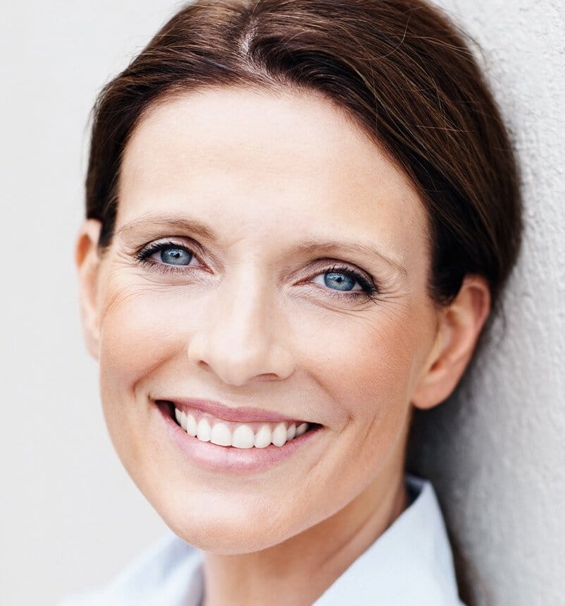 smiling woman with blue eyes and a white shirt leaning against a wall